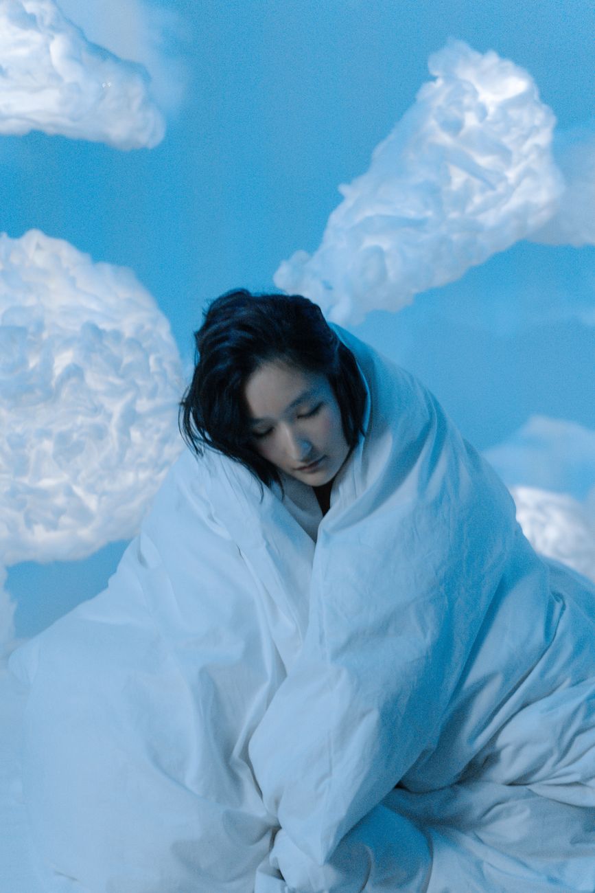 woman in white blanket sitting among clouds